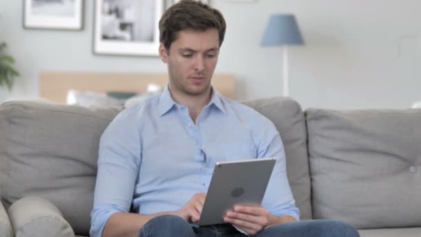 Relaxante jovem bonito comemorando o sucesso no tablet — Vídeo de Stock