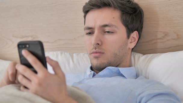 Hombre joven usando Smartphone en la cama — Vídeo de stock
