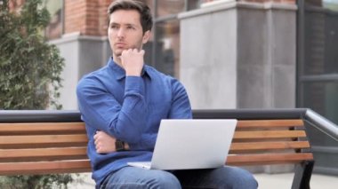 Laptop üzerinde çalışan Pensive genç adam, Bench açık oturma