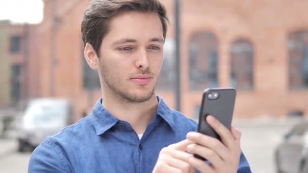 Wow, Portrait extérieur d'un jeune homme surpris utilisant un téléphone intelligent — Video