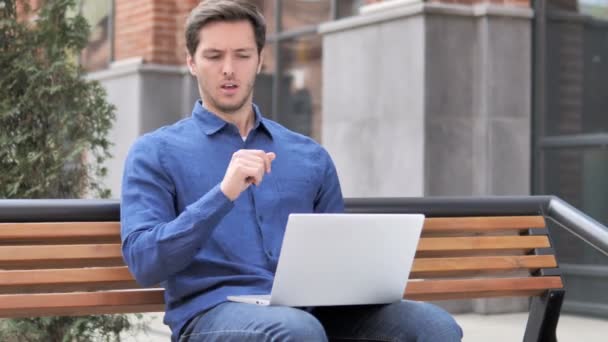 Сидячи на відкритому повітрі молодий чоловік кашляє під час роботи на ноутбуці — стокове відео
