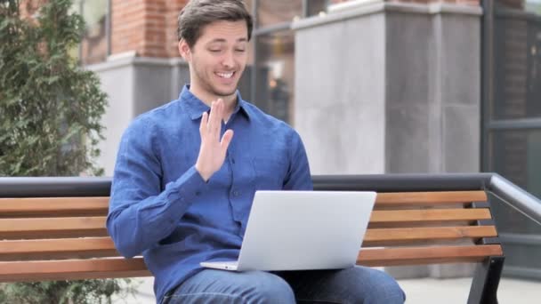 Online videokonverzace na přenosném počítači mladým mužem sedícího na lavici — Stock video