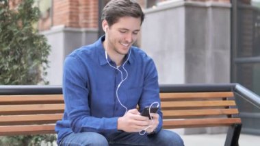 Bench üzerinde otururken akıllı telefonda müzik dinleme genç adam