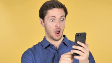 Wow, sarı arka plan üzerinde Smartphone kullanarak sürpriz Casual genç adam