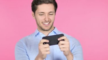 Genç adam pembe arka plan üzerinde Smartphone oyun oynuyor
