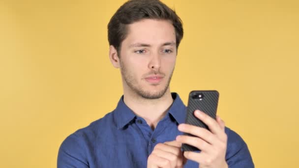 Случайный молодой человек с помощью смартфона на желтом фоне — стоковое видео