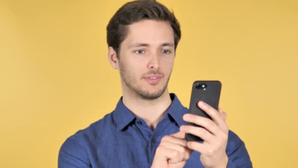 Περιστασιακή νέος άντρας γιορτάζει την επιτυχία, ενώ χρησιμοποιώντας το smartphone σε κίτρινο φόντο — Αρχείο Βίντεο