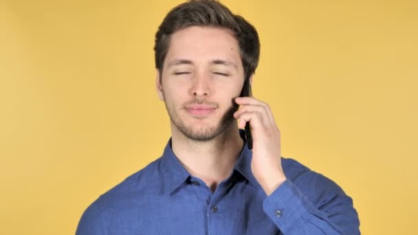 Случайный молодой человек разговаривает по телефону на желтом фоне — стоковое видео