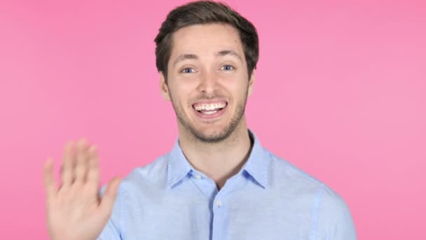 ピンクの背景に歓迎するために手を振る若い男 — ストック動画