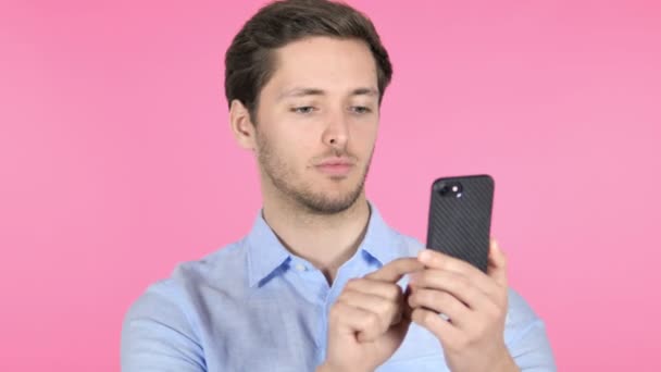 Hombre joven usando Smartphone sobre fondo rosa — Vídeo de stock