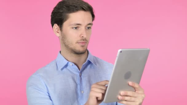 Молодий чоловік святкує успіх на планшеті, рожевому фоні — стокове відео