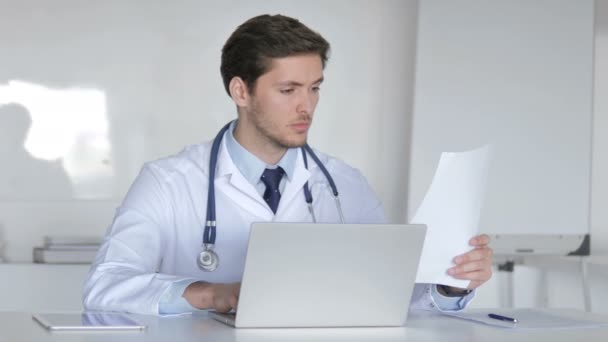 Giovane medico che lavora su computer portatile e documenti medici — Video Stock
