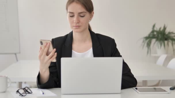 Multitasking ung affärskvinna med hjälp av smartphone och laptop — Stockvideo