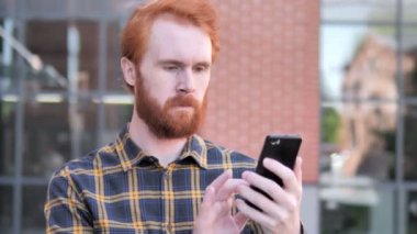 Açık kızıl sakal genç adam heyecan akıllı telefonda başarı için