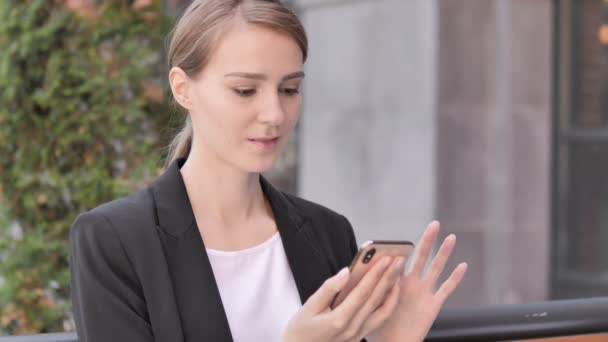 Junge Geschäftsfrau sitzt mit Smartphone im Freien — Stockvideo