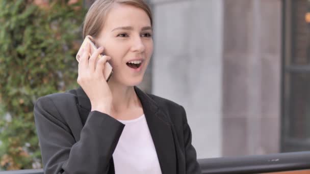 Jonge zakenvrouw praten op telefoon zittend buiten — Stockvideo