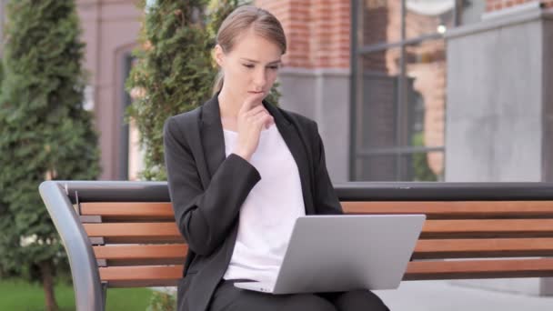 Joven empresaria pensativa que trabaja en el ordenador portátil, sentado al aire libre en el banco — Vídeos de Stock