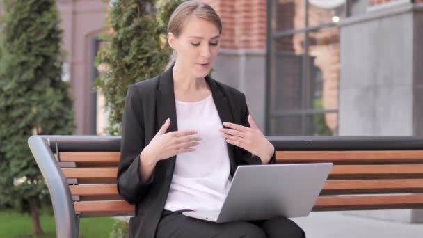 Онлайн видео чат на ноутбуке от молодой предпринимательницы, сидящей на скамейке запасных — стоковое видео