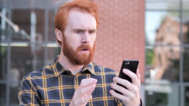 Outdoor rossa barba giovane uomo sconvolto dalla perdita durante l'utilizzo di smartphone — Video Stock