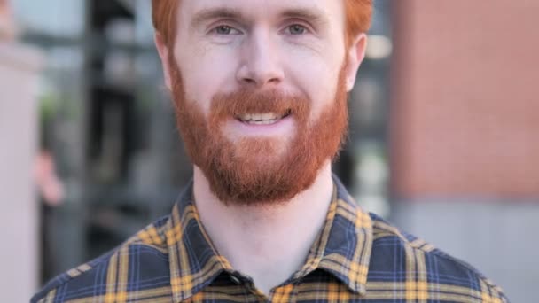 Gros plan de jeune homme barbe rousse souriante, extérieur — Video