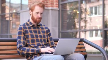 Kızıl Sakal genç adam ofis dışında oturan laptop kutluyor