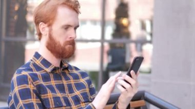 Açık otururken akıllı telefon kullanarak sakal genç adam