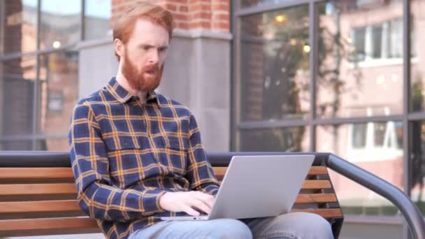 Ruiva barba jovem tosse enquanto trabalhava no laptop ao ar livre — Vídeo de Stock