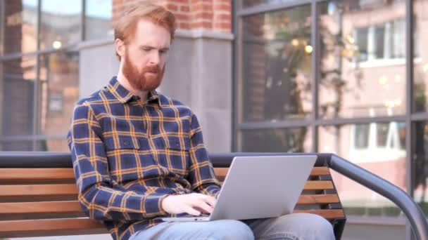 Redhead skägg ung man med ryggvärk arbetar på laptop utomhus — Stockvideo