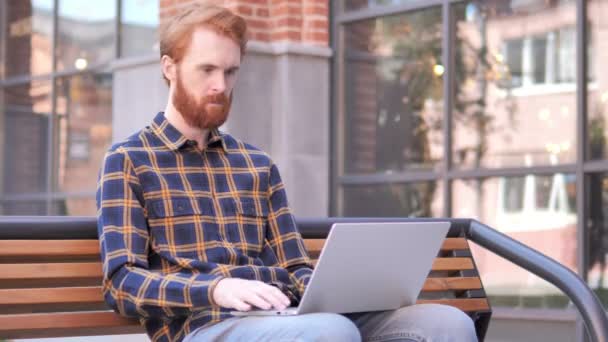 Онлайн відео чат на ноутбуці Рудий Борода молодий чоловік сидить на лавці — стокове відео