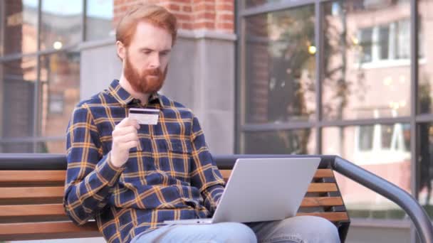 Online vásárlás a vöröshajú szakálla fiatal férfi ül a padon — Stock videók