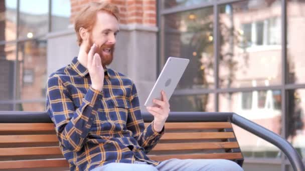 Video chat a Tablet a vöröshajú szakálla fiatal ember ül a padon — Stock videók