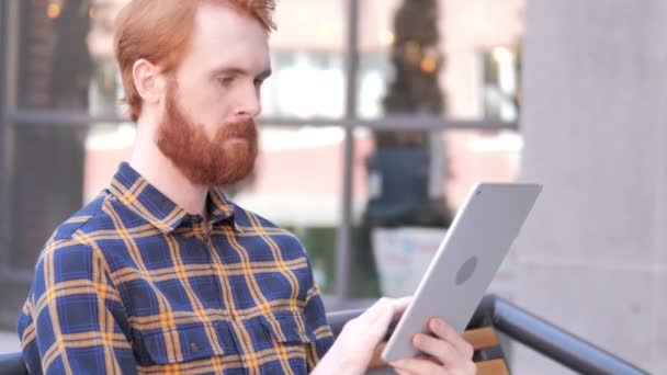 Vousatý mladý muž použití tabletu při sezení venku — Stock video