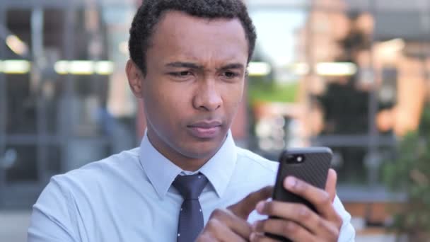 Utomhus afrikansk affärsman upprörd av förlust när du använder smartphone — Stockvideo