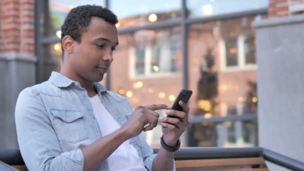 Afrikansk man använder smartphone sittande utomhus — Stockvideo