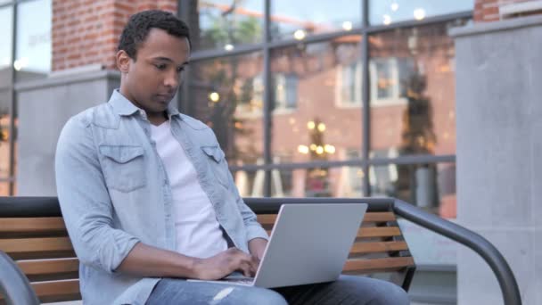 African Man pracujący na laptopie, siedząc na ławce — Wideo stockowe