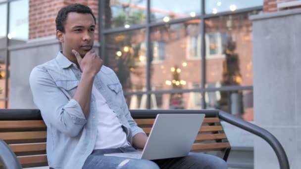 Nachdenklicher Afrikaner arbeitet am Laptop, sitzt auf Bank — Stockvideo