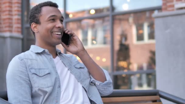 Africano hombre hablando en teléfono sentado al aire libre — Vídeos de Stock