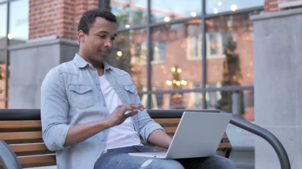 Chat de vídeo en línea en el ordenador portátil por el hombre africano sentado en el banco — Vídeos de Stock