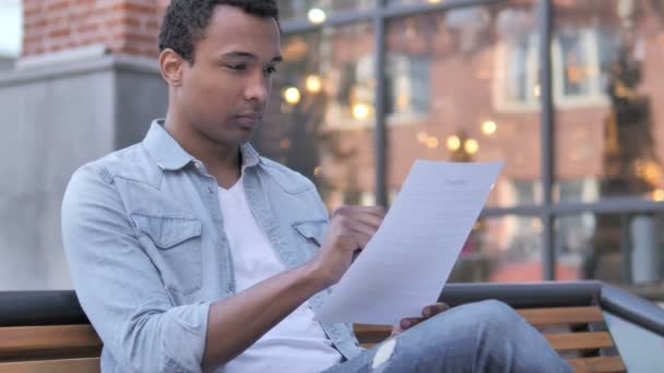 Hombre africano leyendo documentos mientras está sentado al aire libre — Vídeos de Stock
