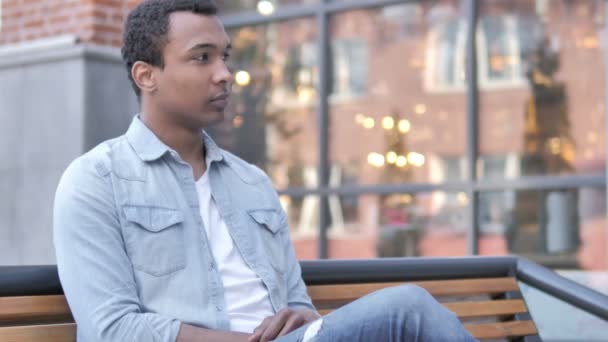 Mladý Afričan s úsměvem při sezení na lavici — Stock video