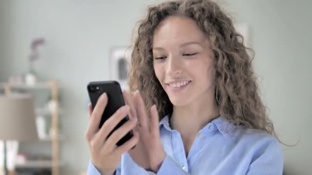 Захоплена кучеряве волосся жінка насолоджується успіхом під час використання смартфона — стокове відео
