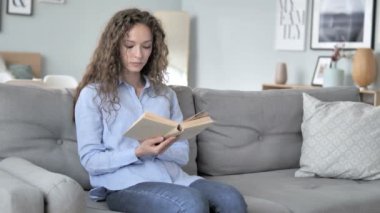 Kanepede otururken kıvırcık saç kadın okuma kitabı