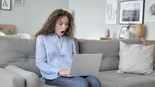 Schockierte Frau mit lockigem Haar arbeitet am Laptop und sitzt auf der Couch — Stockvideo