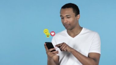 Mavi arka planda Izole Smartphone kullanarak Afrika adam, uçan Smileys, emojis ve sevdikleri