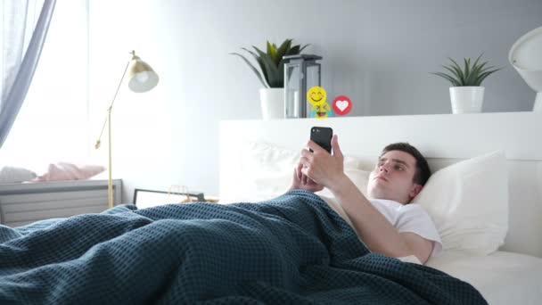Νέος άνθρωπος στο κρεβάτι παρακολουθώντας μια ζωντανή ροή στο smartphone, emoji και του αρέσει — Αρχείο Βίντεο