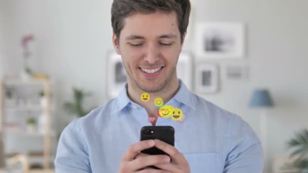 Happy man SMS-berichten op smartphone, vliegende Emoji's, smileys en likes — Stockvideo