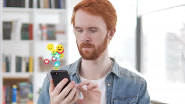 Рудий борода дизайнер за допомогою смартфона, літаючих Emojis, смайлики і любить — стокове відео
