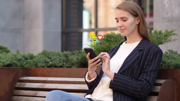 Υπαίθρια καθιστή επιχειρηματίας χρησιμοποιώντας smartphone, ιπτάμενες Σμιλίες, emojis και συμπαθεί — Αρχείο Βίντεο