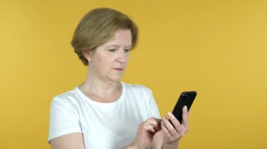 Sarı arka planda Izole Smartphone kullanırken başarı için heyecanlı yaşlı kadın