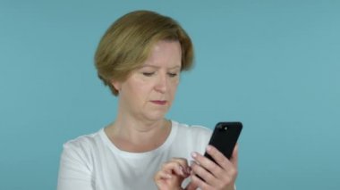 Mavi arka planda Izole Smartphone kullanırken başarı için heyecanlı yaşlı kadın